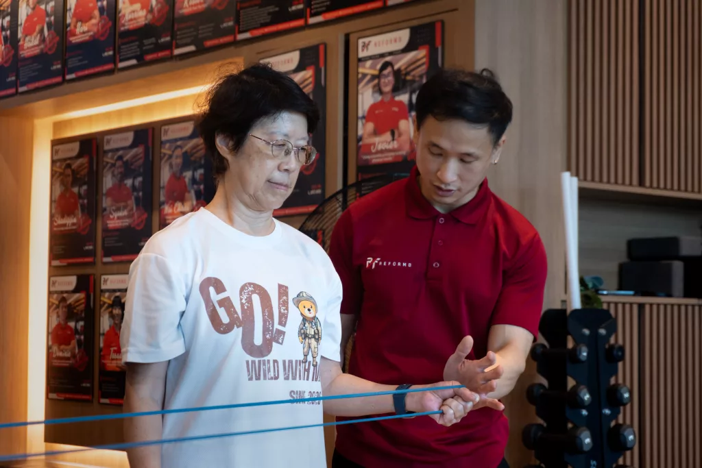 ReFormd Personal Trainer instructing an elderly client on a banded external rotation exercise