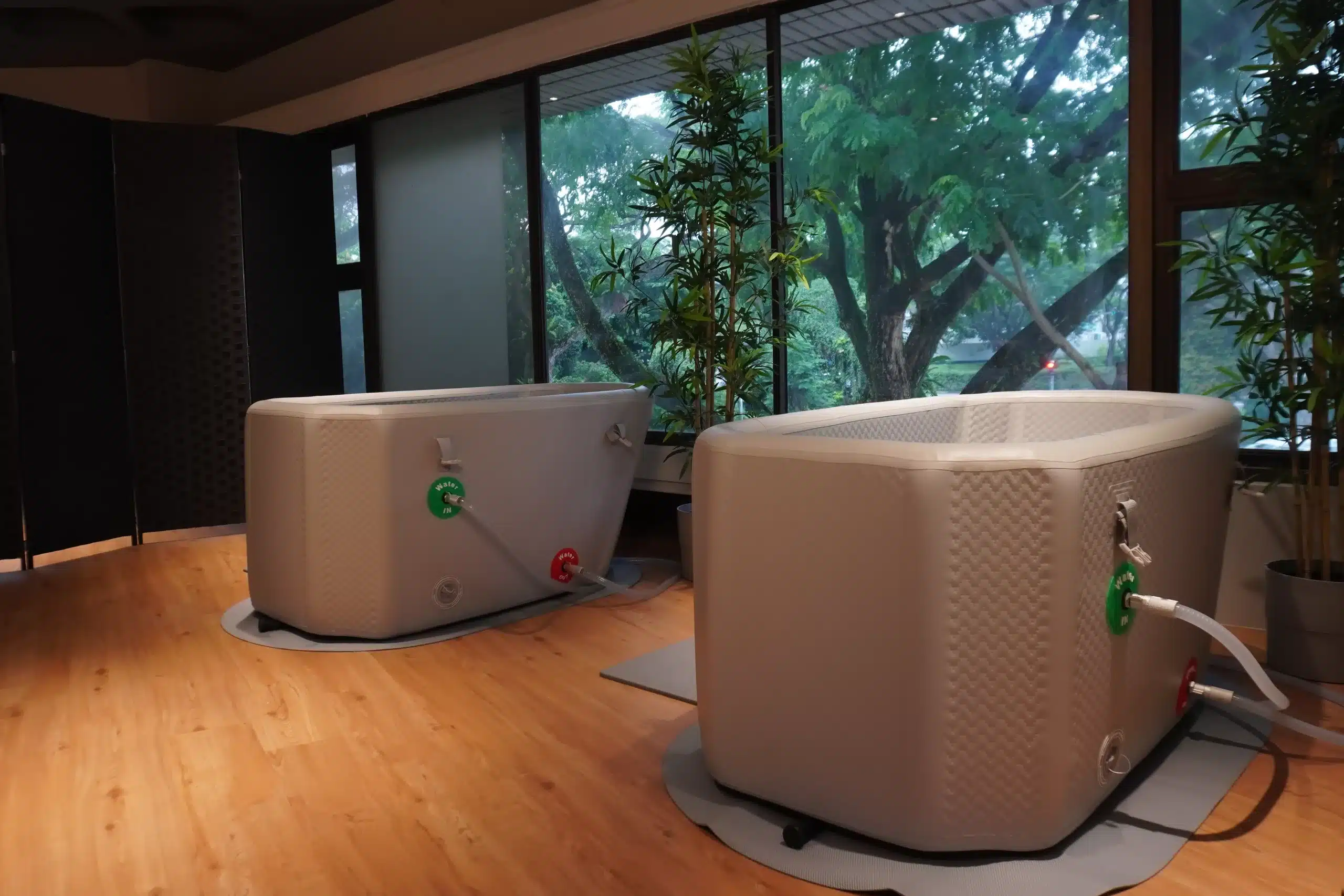 Two Tundra Ice bath tubs with artificial bamboo between them. The glass is slightly foggy due to the heat from the tubs which contributes to an aesthetic photo