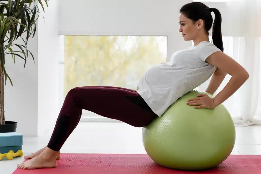 Side view of a young pregnant woman exercising on a fitness ball Side-view-young-pregnant-woman-exercising-fitness-ball
